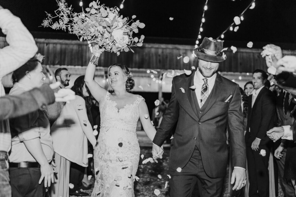 black and white image of couple after getting married, smiling and holding flowers up in the air